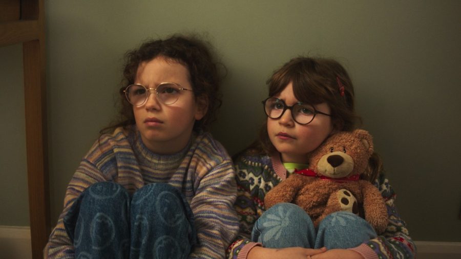 Two young sisters sitting together against a bedroom wall in the Sharps Sisters advert